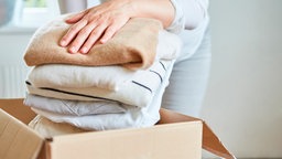Frau packt Kleidung in einen Karton.