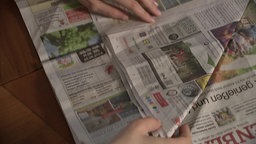 Eine Person faltet eine alte Zeitung.