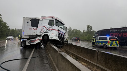 Ein Lkw ist auf einer Mittelleitplanke auf der A3 bei Bad Honnef. Im Hintergrund steht die Polizei. 