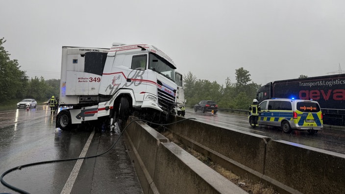 Ein Lkw ist auf einer Mittelleitplanke auf der A3 bei Bad Honnef. Im Hintergrund steht die Polizei. 