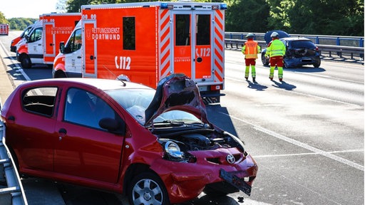 Ein an der Front beschädigtes Auto steht rückwärts auf der Autobahn, im Hintergrund Rettungswagen