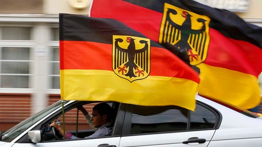 Ein Auto mit Deutschlandflaggen fährt durch eine Stadt
