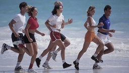 Eine Gruppe Menschen joggt in Sportkleidung am Strand entlang