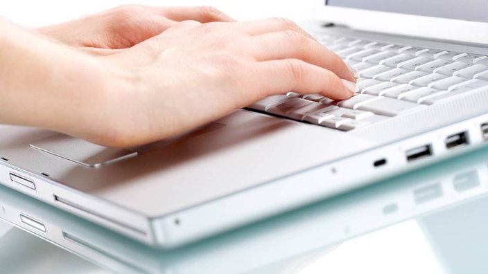 Ein grauer Laptop steht auf einem Tisch. Zwei Hände tippen auf der Tastatur