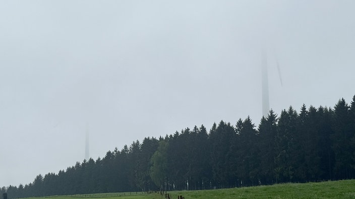 Zwei Windräder stehen im Nebel und drehen sich.