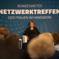 Vor einem blauen Hintergrund sitzen drei Frauen und schauen ins Publikum.