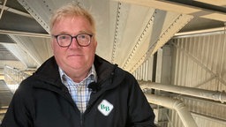 Der Agrarberater mit Brille steht vor einem Getreiderohr des Agrarhandel