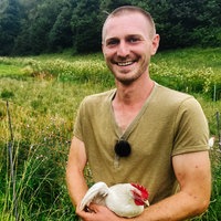 Lucas Wilhelm hält ein weißes Huhn in der Armen. Hinter ihm ist eine Wiese mit weiteren Hühnern