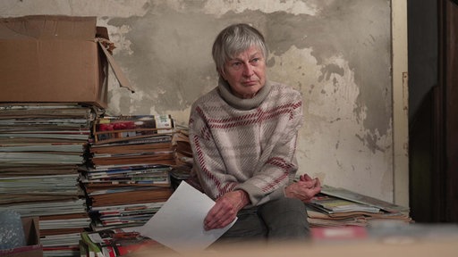 Marianne Lütkehölter sitzt auf und neben großen Stapeln mit Zeitschriften über Traktoren.