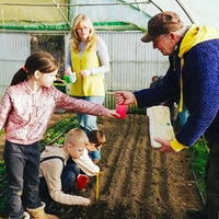 Vier Personen, eine Frau, ein Mann und zwei Kinder, stehen in einem Gewächshaus und bringen Saatgut ins Feld.