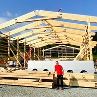 Philipp Henk vor einem großen Holzgerüst eines Stalls. Im Hintergrund einige Bauarbeiter.