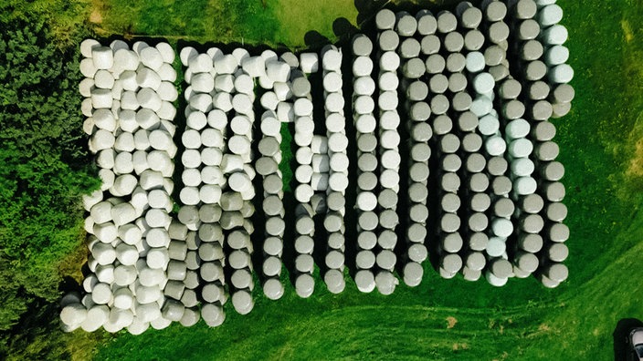Vogelperspektive auf zahlreiche weiße und graue Ballen, in denen Gras konserviert wird