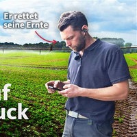 Michael Overkämping schaut auf sein Handy. Im Hintergrund ein grüner Acker
