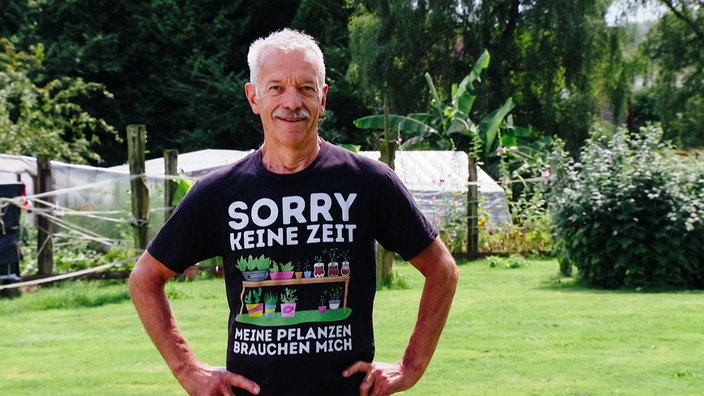 Ein älterer Mann in schwarzem T-Shirt mit dem Aufdruck "Sorry keine Zeit, meine Pflanzen brauchen mich"