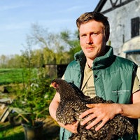 André Wallich steht draußen und hält eine Henne in den Armen. Er lächelt.