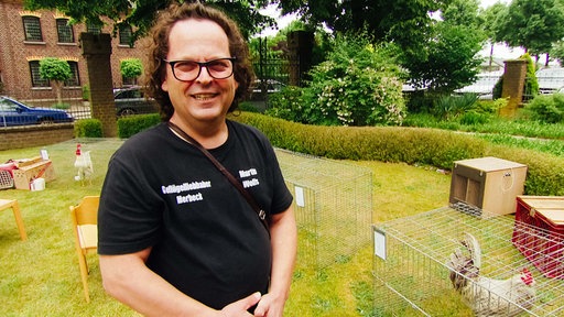Ein Mann mit Brille und braunen Haaren im Portrait. Er trägt ein schwarzes T-Shirt. 