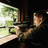 Martina Rohn steht an einer der Öffnungen ihres Hochsitzes. Mit ihrem Gewehr zielt sie in die Ferne.
