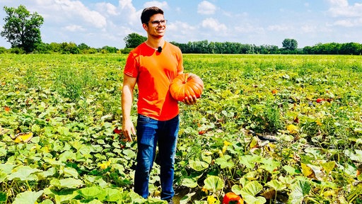 Max Bieger steht auf einem Feld und hält einen Kürbis im Arm.