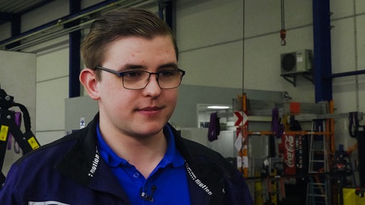 Landmaschinenmechatroniker Konstantin Winkler steht in blauer Arbeitsjacke in einer Werkstatt