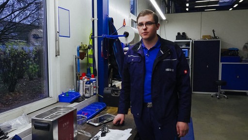 Landmaschinenmechatroniker Konstantin Winkler steht in blauer Arbeitsjacke in einer Werkstatt
