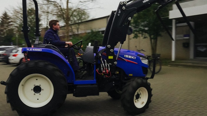 Ein Mann fährt auf einem blauen Traktor über einen Parkplatz