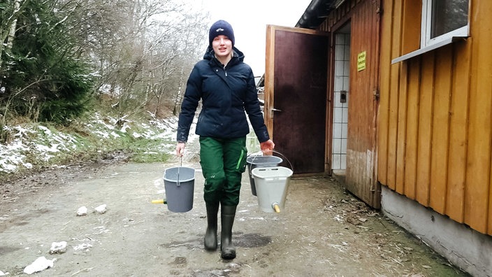 Annika Braach steht neben dem Gatter der Kälbchen und hängt die Eimer zum Trinken an den Zaun.