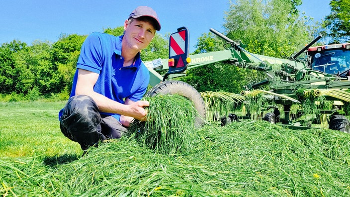 Ein Mann hockt auf einer Wiese und hält frisch gemähtes Gras in der Hand.