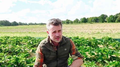 Ein Mann spricht auf einem Feld in die Kamera.