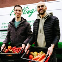 Johannes Becker links und Daniel Neumann rechts vor einem ihrer Gemüse-Transporter. Beide halten eine Gemüsekiste in der Hand.