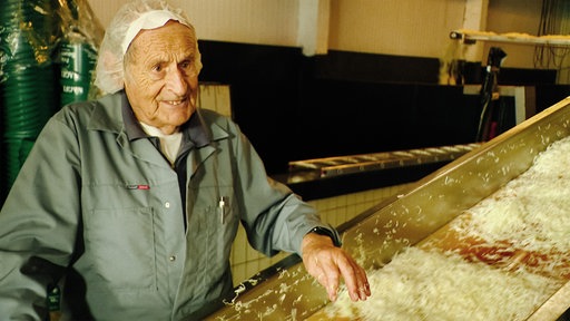 Franz Stieger steht hinter einer Maschine für die Sauerkrautherstellung. Er trägt Arbeitskleidung.