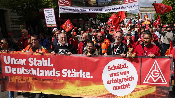 Gruppe von Demonstrierenden mit roten Fahnen und Bannern, vorne rotes Banner mit weißer Aufschrift 'Unser Stahl. Deutschlands Stärke.' und 'Schützt, was uns erfolgreich macht!'