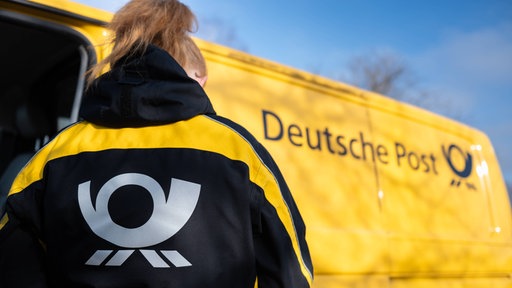 Eine Briefträgerin vor einem gelben Deutsche Post-Fahrzeug 