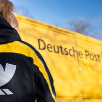 Eine Briefträgerin vor einem gelben Deutsche Post-Fahrzeug 