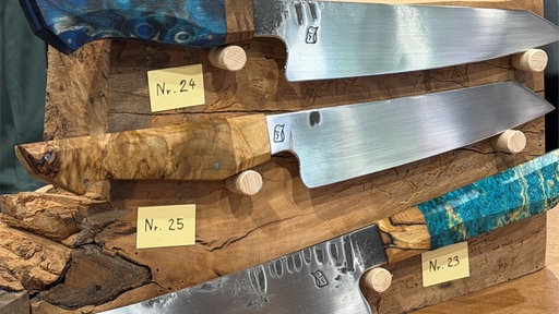 drei Messer hängen zur Ausstellung an einem Holzbrett