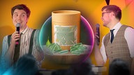 Die Science Cops Jonathan und Max stehen auf einer Bühne und halten ein Mikro in der Hand. Zwischen ihnen ist eine Dose zu sehen, davor liegen grüne Kapseln.