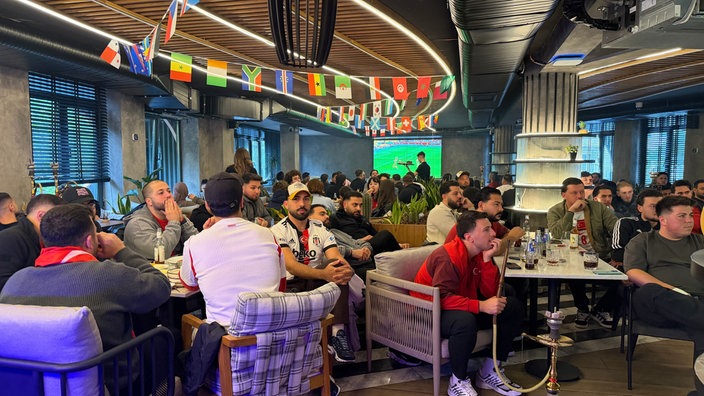 Personen sitzen in einem Restaurant und schauen das Fußballspiel.