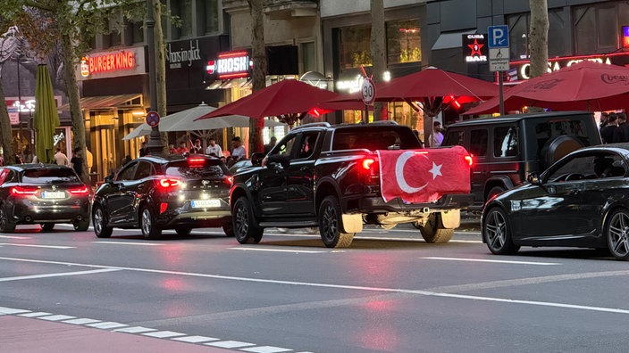 Schwarze Autos haben auf einer Straße gehalten. Eines der Autos hat eine Türkei-Flagge am Kofferauf befestigt.