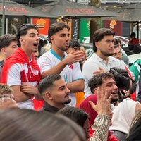 Drei junge Männer stehen zwischen weiteren Fußballfans und schauen das WM-Spiel 