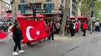 Zwei Personen haltenauf der Straße stehend eine große Türkei-Flagge hoch. Im Hintergrund sind weitere Fans zu sehen.