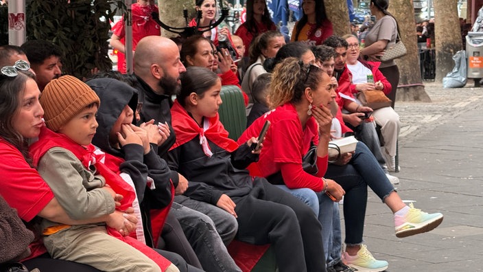 Fußballfans schauen draußen auf einer Bank sitzend das WM-Spiel 